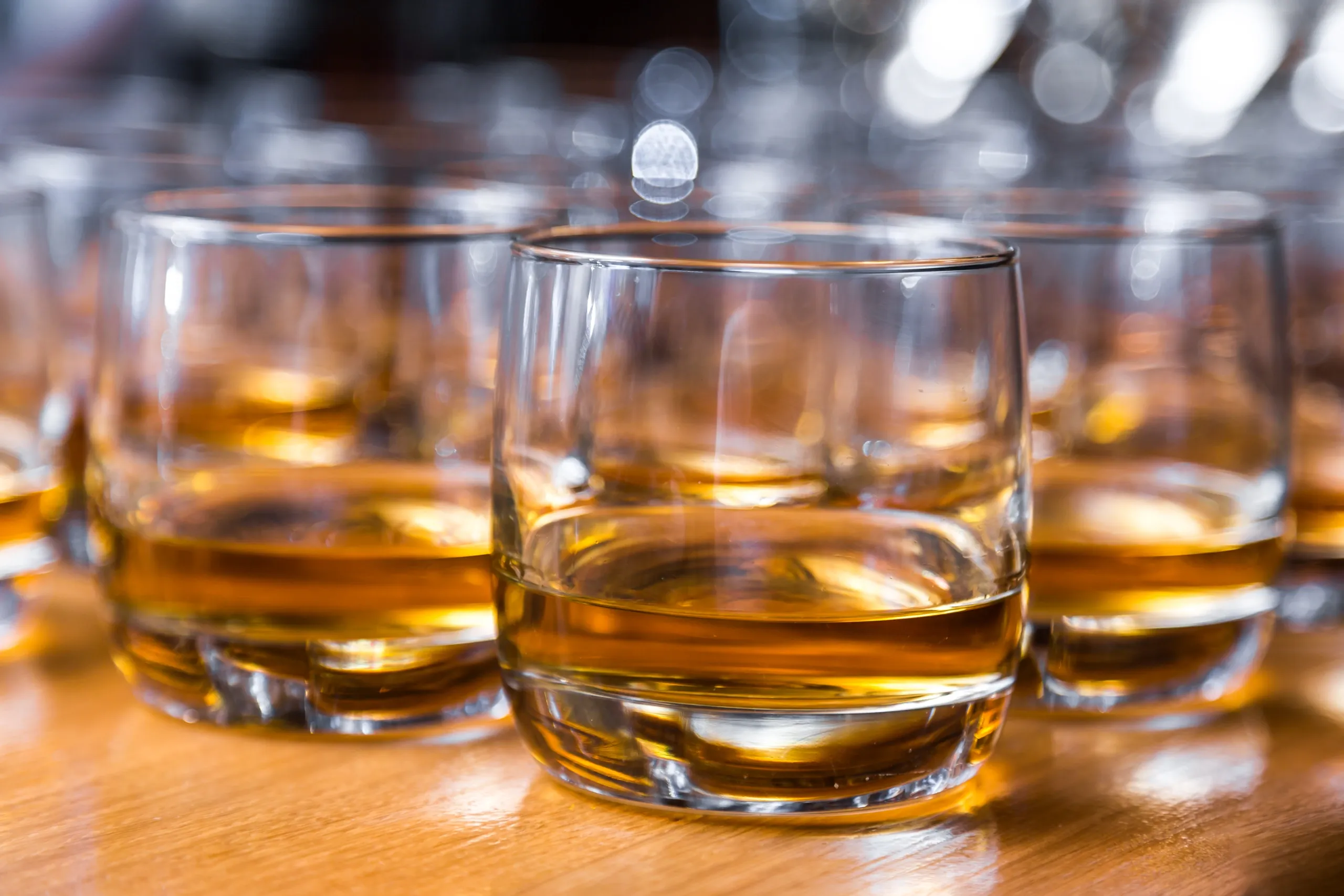 Glasses of whiskey on wooden table.